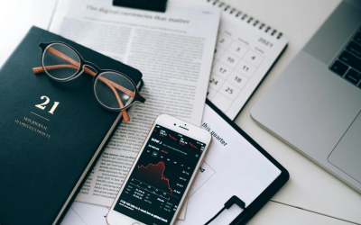 smartphone displaying a stock market chart lying on documents next to a laptop on the desk